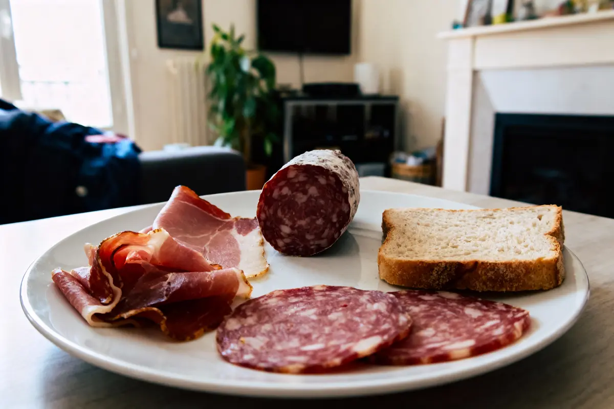 Assiette de charcuterie avec jambon, saucisson et tranche de pain dans un salon.