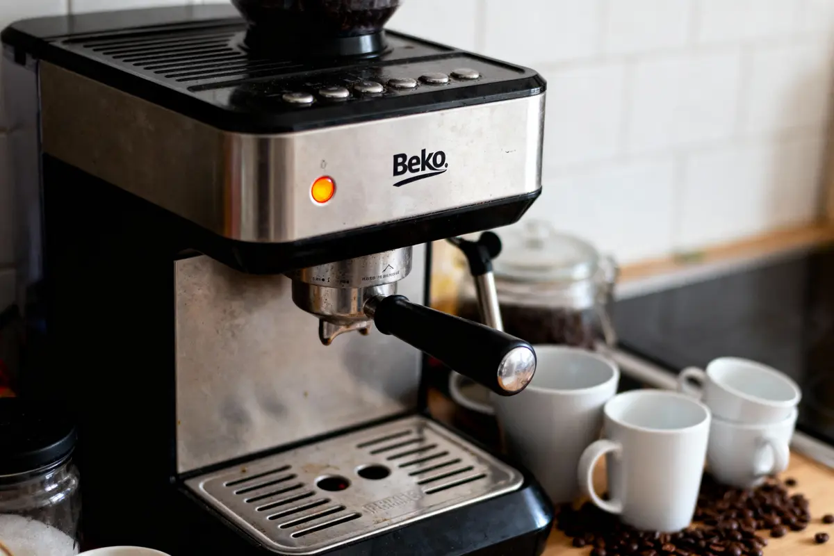 Machine à café Beko avec tasses blanches et grains de café sur le plan de travail.