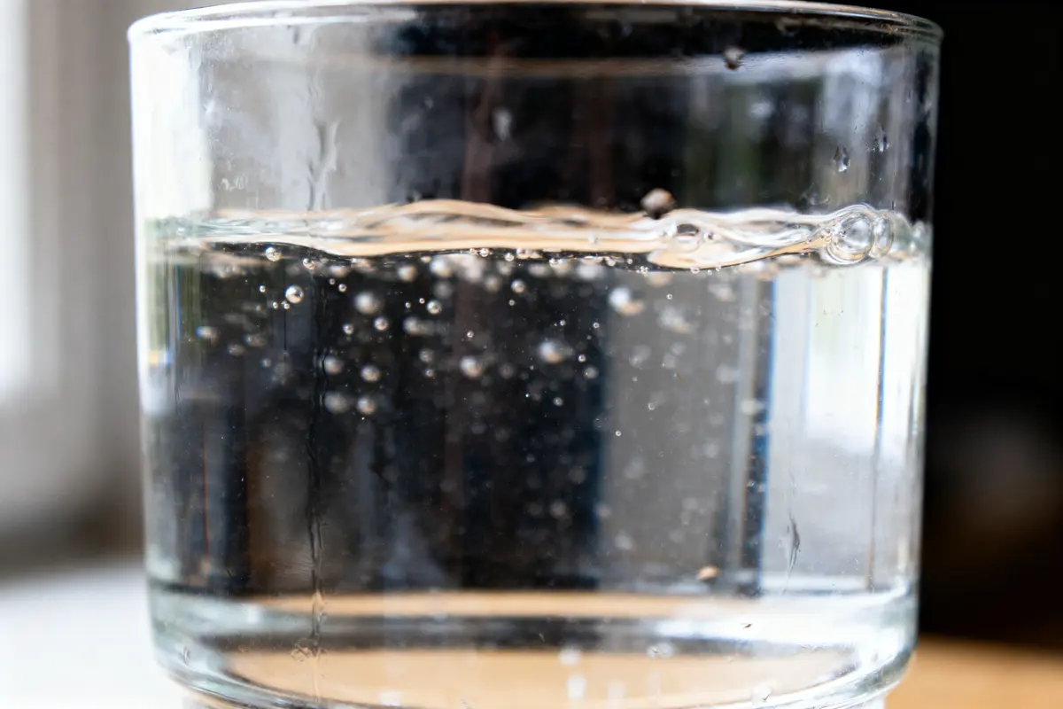 Verre d'eau gazeuse sur table avec bulles visibles à l'intérieur. Fond flou, lumière naturelle.