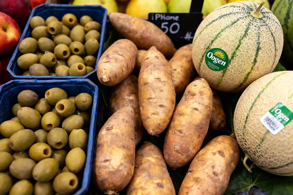 Patates douces, melons Ogen, olives vertes en barquettes, étiquette humoristique "iPhone 50" visible.