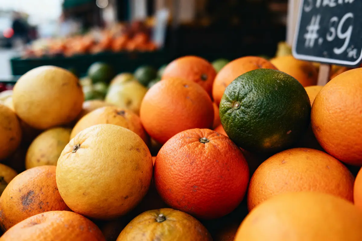 Oranges et citrons empilés sur un marché, avec une étiquette de prix visible en arrière-plan.