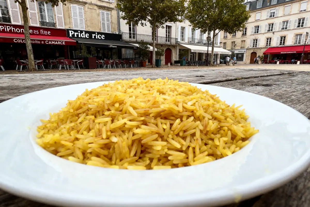 Assiette de riz jaune sur une table en bois avec bâtiments et cafés en arrière-plan.