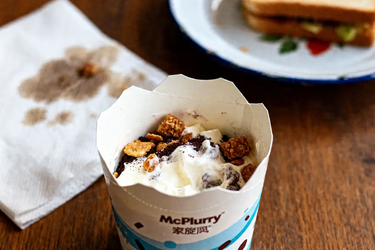 Dessert McFlurry avec topping croquant sur table en bois près d'un sandwich et serviette tachée