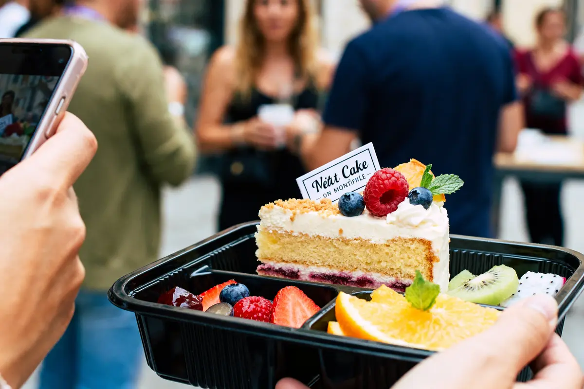 Personne photographie un gâteau aux fruits dans une boîte my bento cake devant des gens