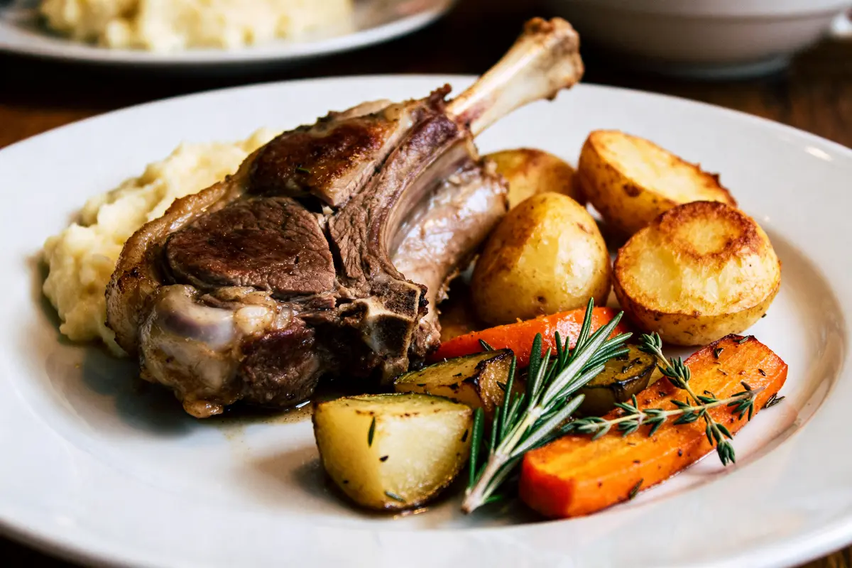 Assiette avec accompagnement du gigot d'agneau : pommes de terre, carottes, herbes aromatiques